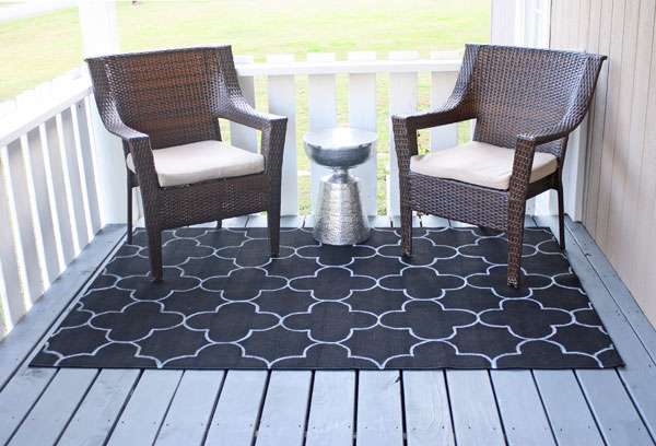 Black quatrefoil patterned outdoor rugs on a porch with two wicker chairs.