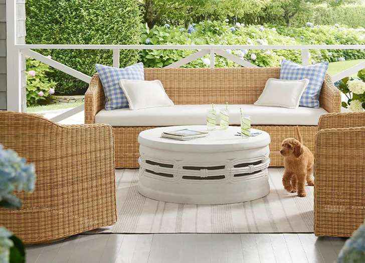 Wicker outdoor furniture with a light striped Outdoor Rug and white coffee table on porch.