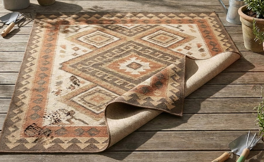 Tribal patterned outdoor rugs on a wooden deck, partially lifted, with gardening tools.