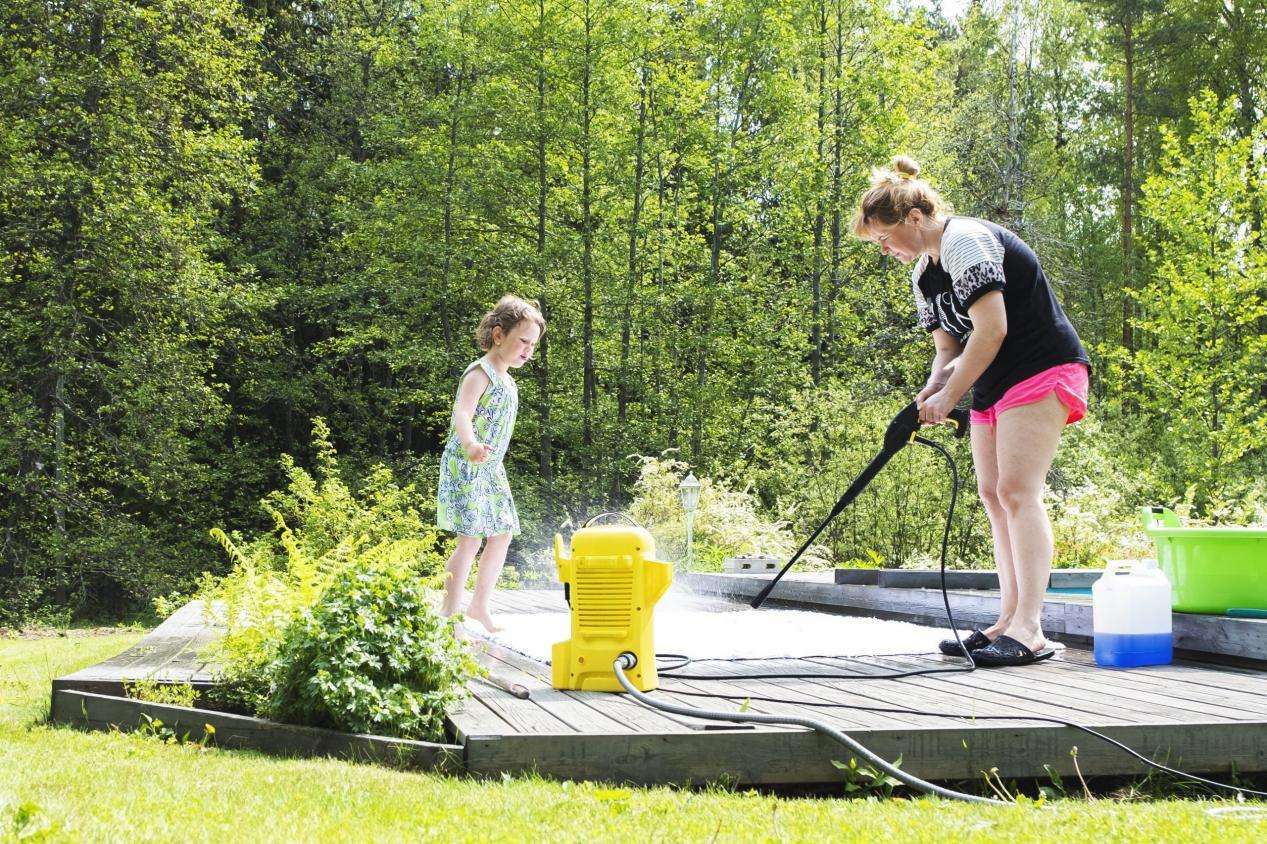 Mother and child cleaning large outdoor rugs on a sunny wooden deck.