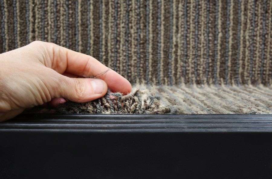 Hand lifting a section of a durable ribbed brown outdoor rugs, showing its construction.